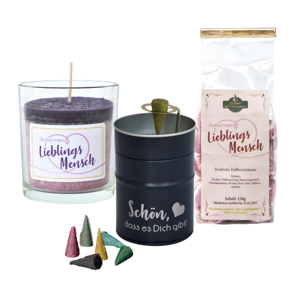 Das Geschenkset „Lieblings Mensch“ von Original Crottendorfer umfasst eine lila Stearinkerze im Glashalter mit der Aufschrift „Du bist mein Lieblingsmensch“, Wildblumen Duft Räucherkerzen in einer Metalldose und Erdbeerbonbons, alles wunderschön arrangiert auf weißem Hintergrund.