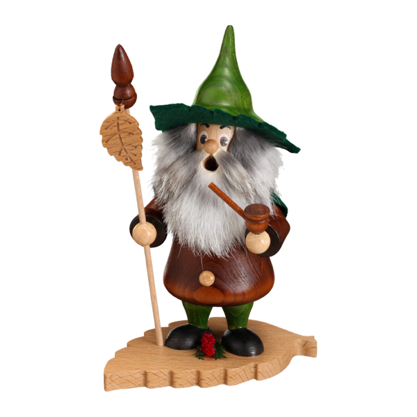 Das Blattwichtel Buchenblatt von DWU Drechselwerkstatt Uhlig ist eine Räuchermann-Figur aus Holz, die einen skurrilen bärtigen Mann aus dem Erzgebirge darstellt, der einen grünen Hut trägt. Er hält einen mit Blättern verzierten Stab und eine Pfeife und steht auf einem blattförmigen Sockel mit traditioneller roter Volkskunstdekoration.