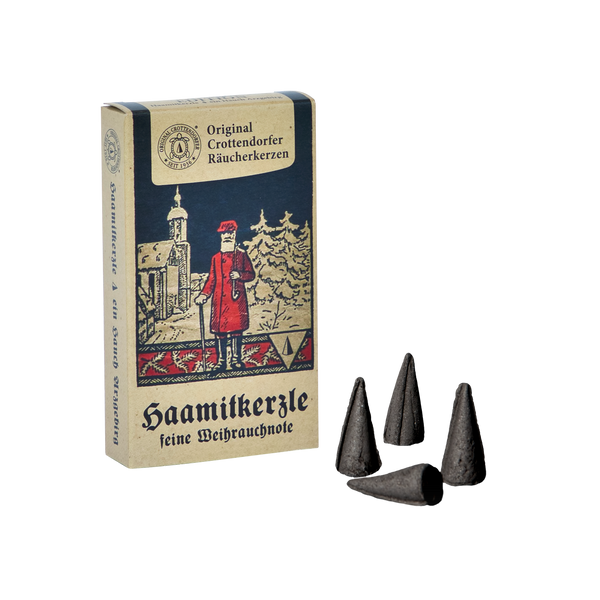 Abgebildet ist eine Schachtel Original Crottendorfer Räucherkerzen „Räucherkerzen Nostalgie Edition Haamitkerzle“, die eine dezente Weihrauchnote verströmt. Die Packungsillustration zeigt eine rot gekleidete Person mit einem Stab, umrahmt von Bäumen und einer Kirche. Daneben liegen vier schwarze Zapfen, die auf ihre aromatische Anziehungskraft hinweisen.