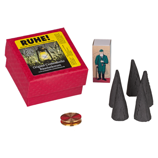 Eine „RUHE!“-Box von Original Crottendorfer Räucherkerzen mit der Abbildung eines Mannes, vier schwarzen kegelförmigen Räucherkegeln (Räucherkerzen) und einer runden, goldenen Messingschale ist auf weißem Hintergrund abgebildet.