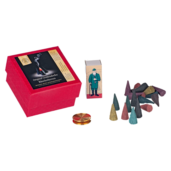 Die Geschenkbox „Wunschduft“ von Original Crottendorfer Räucherkerzen enthält eine rote Box mit bunten Räucherkerzen und eine kleine goldene Messingschale. Auf einer kleineren Packung daneben ist ein Mann in Grün abgebildet, der die Tradition des Weihrauchverbrennens darstellt.