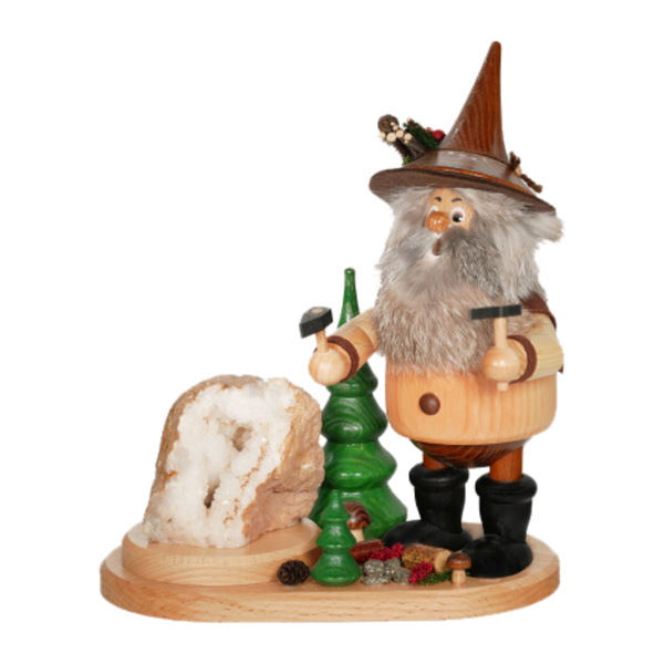 Der Erzwichtel Hauer der DWU Drechselwerkstatt Uhlig ist eine hölzerne Räuchermann-Figur, die einen bärtigen Mann mit spitzem Hut darstellt, der Werkzeuge neben einem grünen Baum und einem Kristallfelsen hält, mit Tannenzapfen und Dekorationen zu seinen Füßen.