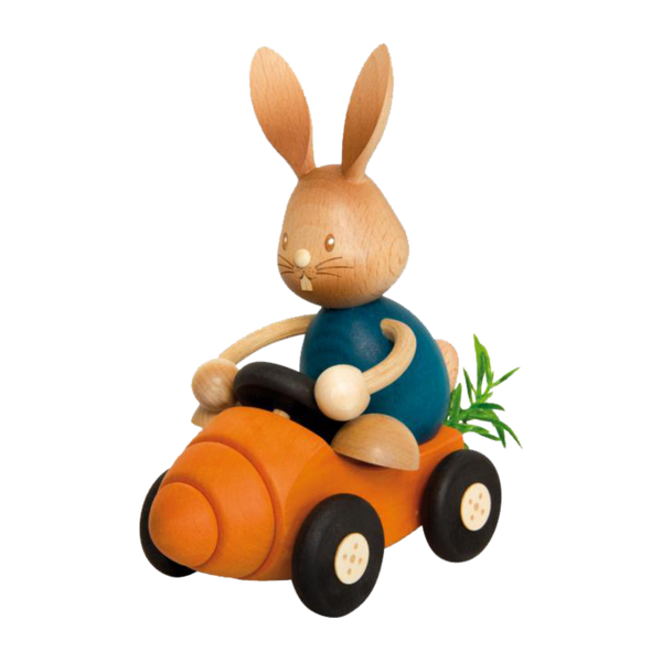 Der Stupsi Hase mit Möhrenflitzer von Drechslerei Kuhnert ist ein bezaubernder Holzhase, der ein orangefarbenes, karottenförmiges Auto mit schwarzen Rädern, langen Ohren, einer blauen Karosserie und leuchtend grünen Blättern auf der Rückseite des Fahrzeugs fährt.