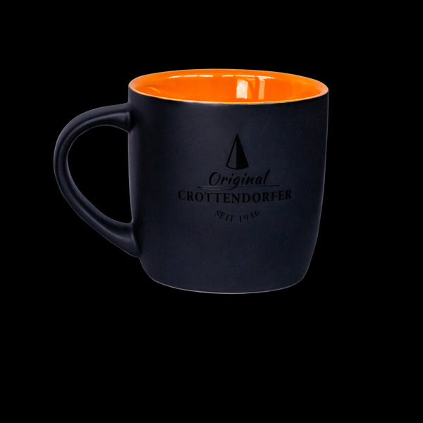 Die Keramiktasse matt von Original Crottendorfer Räucherkerzen hat eine schwarze Außenseite mit einer leuchtend orangefarbenen Innenseite und fasst 300 ml. Sie präsentiert sich elegant vor einem schwarzen Hintergrund und zeigt an der Seite das Logo und den Text „Original Cröttendorfer seit 1946“.