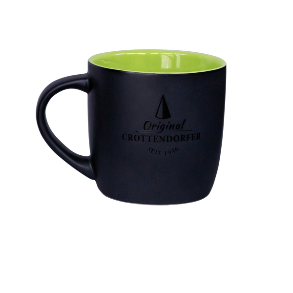 Die Keramiktasse matt hellgrün/schwarz von Original Crottendorfer Räucherkerzen hat eine spülmaschinenfeste mattschwarze Außenseite, eine hellgrüne Innenseite und zeigt elegant „Original Crottendorfer seit 1946“ mit einem dreieckigen Logo an der Seite.
