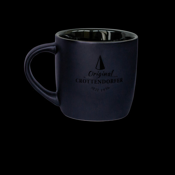Eine mattschwarze Keramiktasse (300 ml) mit glänzender Innenseite steht auf schwarzem Hintergrund. Sie trägt das Logo „Original Crottendorfer Seit 1948“ und ein Tannenbaum-Design. Spülmaschinenfest und leicht zu reinigen, ist sie von Original Crottendorfer Räucherkerzen.