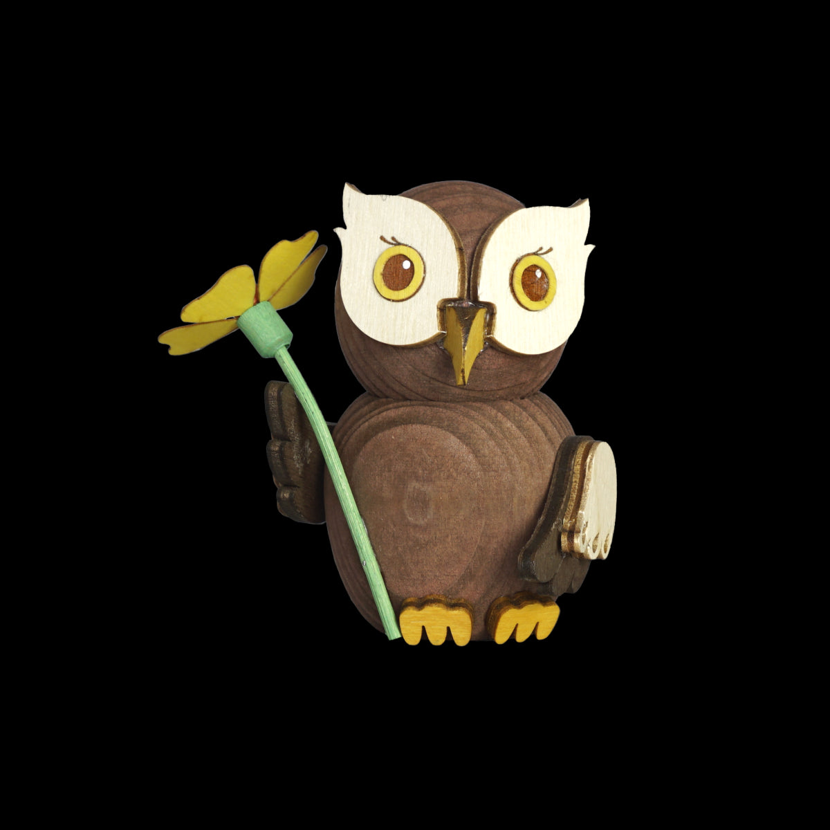 Die Mini Eule Gratulant von Drechslerei Kuhnert ist eine handgefertigte Holzeule mit weißem Gesicht, gelben Füßen und einem gelben Gänseblümchen mit grünem Stiel auf schwarzem Grund. Dieses charmante Stück ist ein Beispiel für die Schönheit nachhaltiger Holzfiguren.