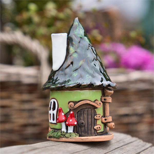 Das Räucherhaus Keramik Pilzhaus grün von Original Crottendorfer ist ein skurriles Keramik-Räucherhaus mit grünem Kegeldach, weißem Schornstein, runder Holztür, Fenstern und rot-weißen Pilzen - handgefertigt und im Freien aufgestellt.