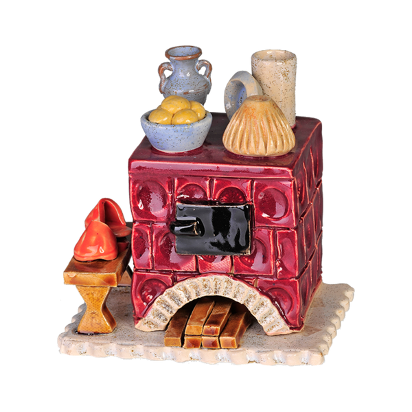 Der Keramik-Räucherofen Mini eckig, altrosa von Keramikwerkstatt Carola Busch ist ein handgefertigtes Keramikmodell eines traditionellen Lehmofens mit roten Kacheln, auf dem kleine Töpfe, Brot und Obst stehen. Ein Paar rote Schuhe steht auf einer kleinen Bank neben diesem charmanten Räucherofen.
