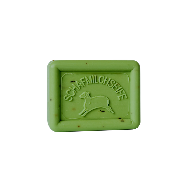 Eine grüne, rechteckige Tafel Ovis Schafmilchseife Kräutersalbe mit der Gravur eines bezaubernden Schafs und dem Wort „Schafmilchseife“ ruht elegant auf schwarzem Hintergrund und verspricht, Ihre Haut mit seiner hautpflegenden Formel zu verwöhnen.