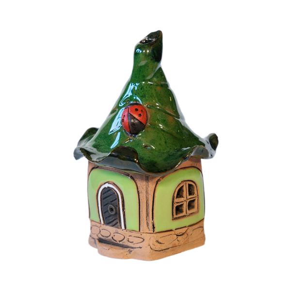 Das Original Crottendorfer Räucherhaus Keramik mini grün mit Marienkäfer hat ein skurriles Design mit einem grünen, gewellten Dach, auf dem ein rot-schwarzer Marienkäfer sitzt. Es hat eine blassgrüne Außenseite, eine Holztür, ein rundes Fenster und ruht auf einem Steinsockel für eine auffällige Präsentation.